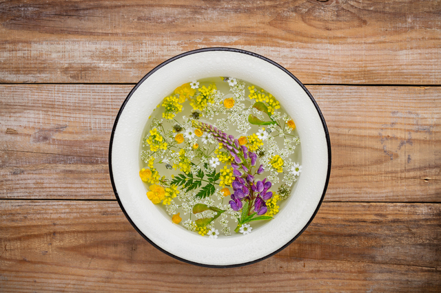 Classic washbowl with water and floating wildflowers and herbs on an old wooden background